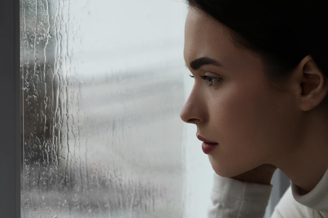 Melancholic young woman watching rain through window, closeup with space for text. Loneliness concept